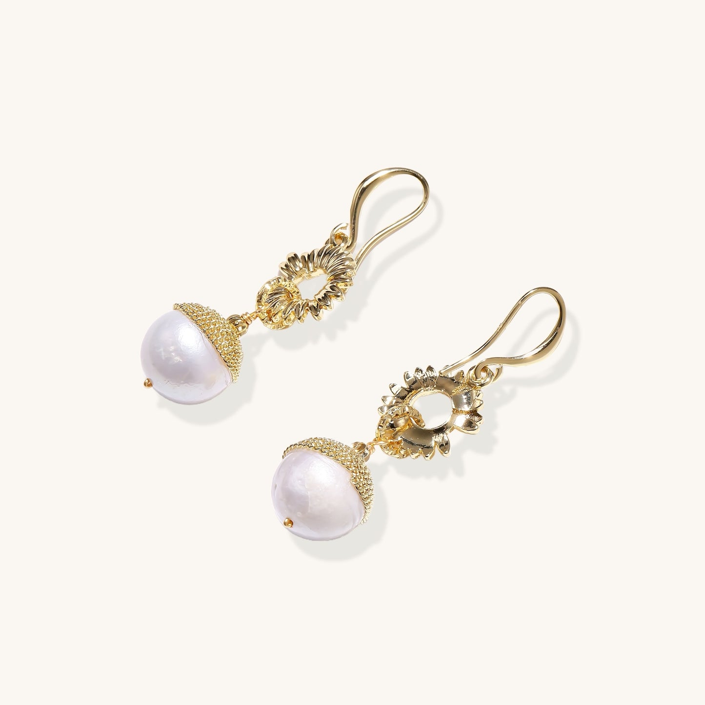 Gold-plated sunburst flower earrings with baroque pearl drops and textured metal caps on neutral background.