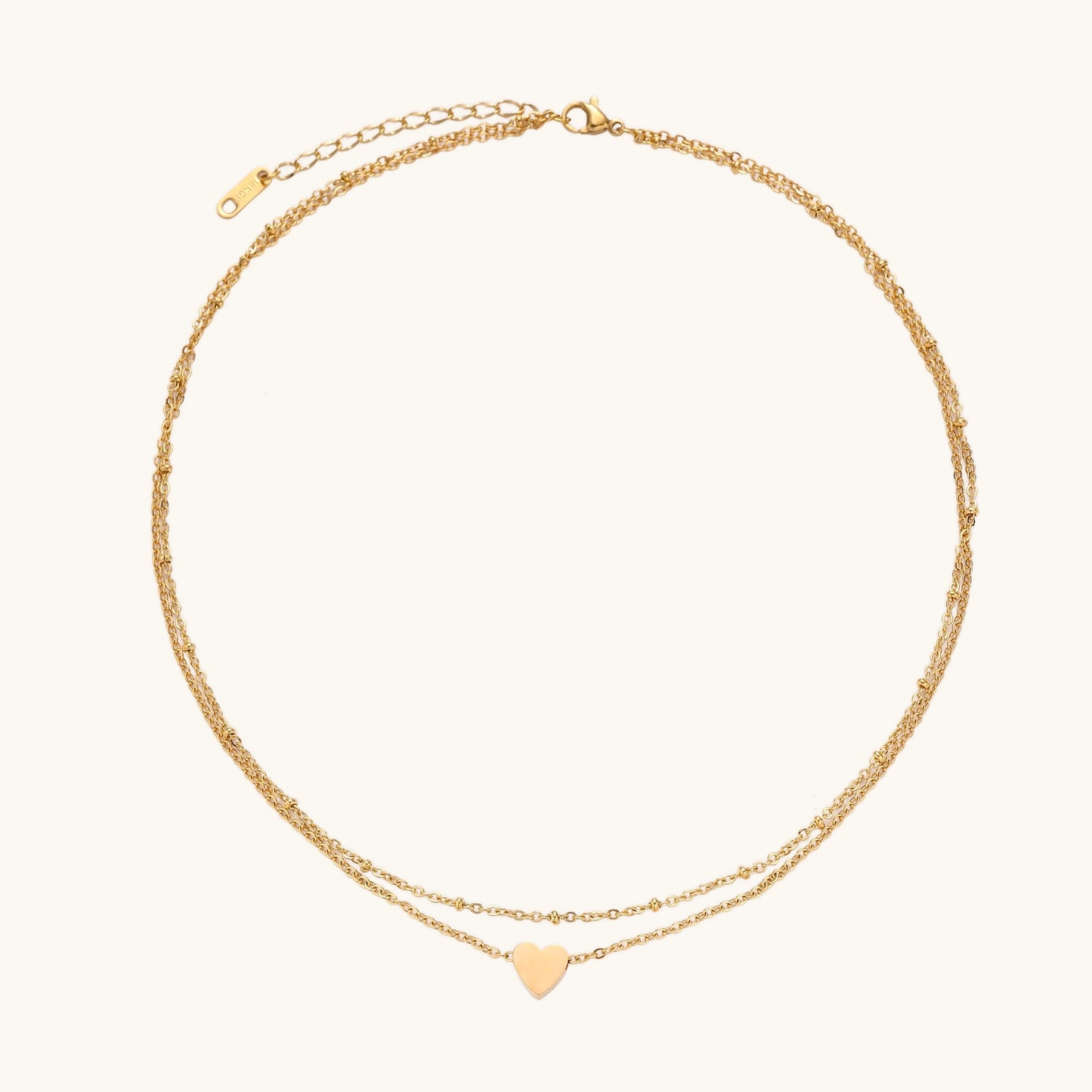 Two-layer gold-plated stainless steel necklace with small heart pendant displayed on beige background