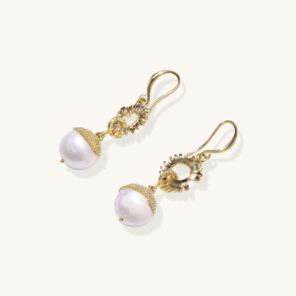 Gold-plated sunburst flower earrings with baroque pearl drops and textured metal caps on neutral background.