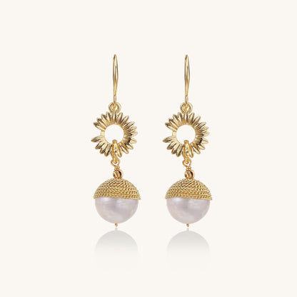 Gold-plated sunburst flower earrings with baroque pearl drops and textured metal caps on neutral background.