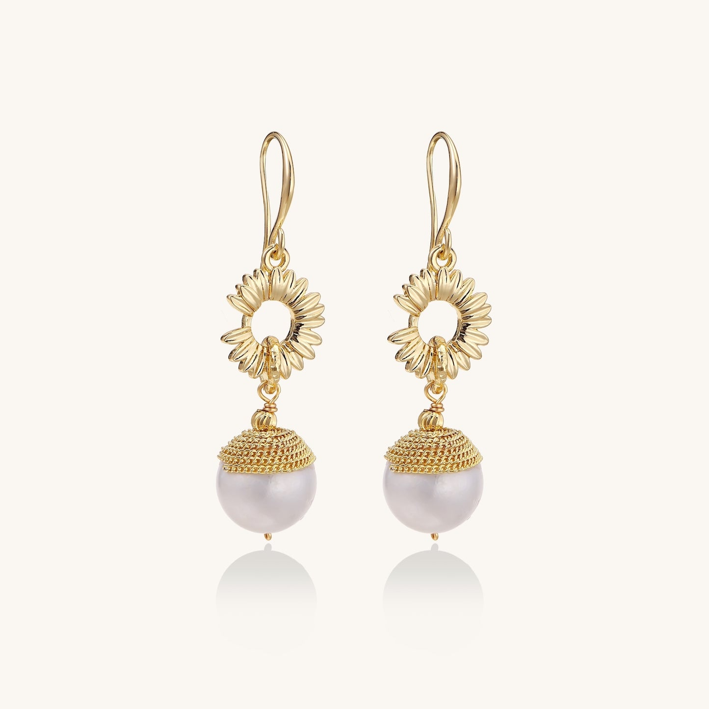Gold-plated sunburst flower earrings with baroque pearl drops and textured metal caps on neutral background.