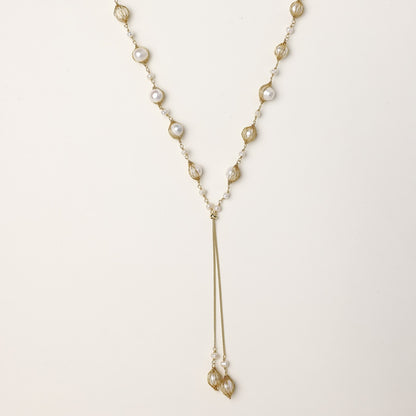 Long gold-plated lariat necklace with wire-wrapped freshwater pearls and chain tassel detail on cream background.