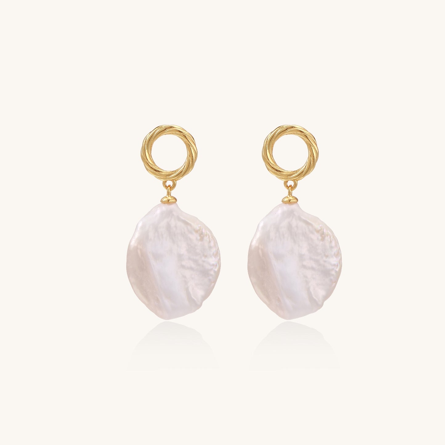 Gold-plated twisted stud earrings with large blush baroque pearls hanging elegantly on white background.