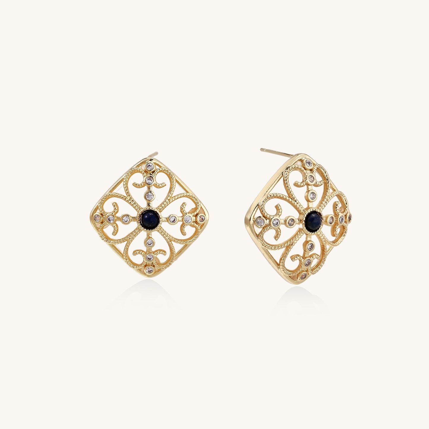 Ornate 18K gold plated stud earrings with intricate filigree design and central lapis lazuli stones on cream background.