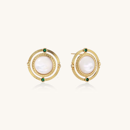 Close-up of gold-plated circular earrings with white mother-of-pearl centers and green zirconia accents on cream background.