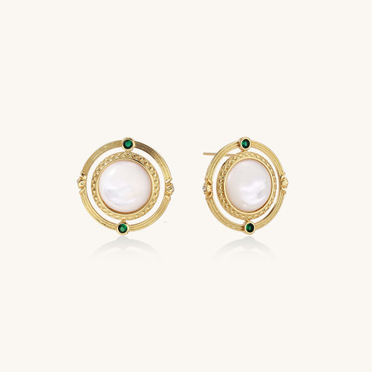 Close-up of gold-plated circular earrings with white mother-of-pearl centers and green zirconia accents on cream background.