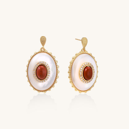 Gold-plated drop earrings with oval mother-of-pearl stones, central red gemstones, and crystal accents on white background.