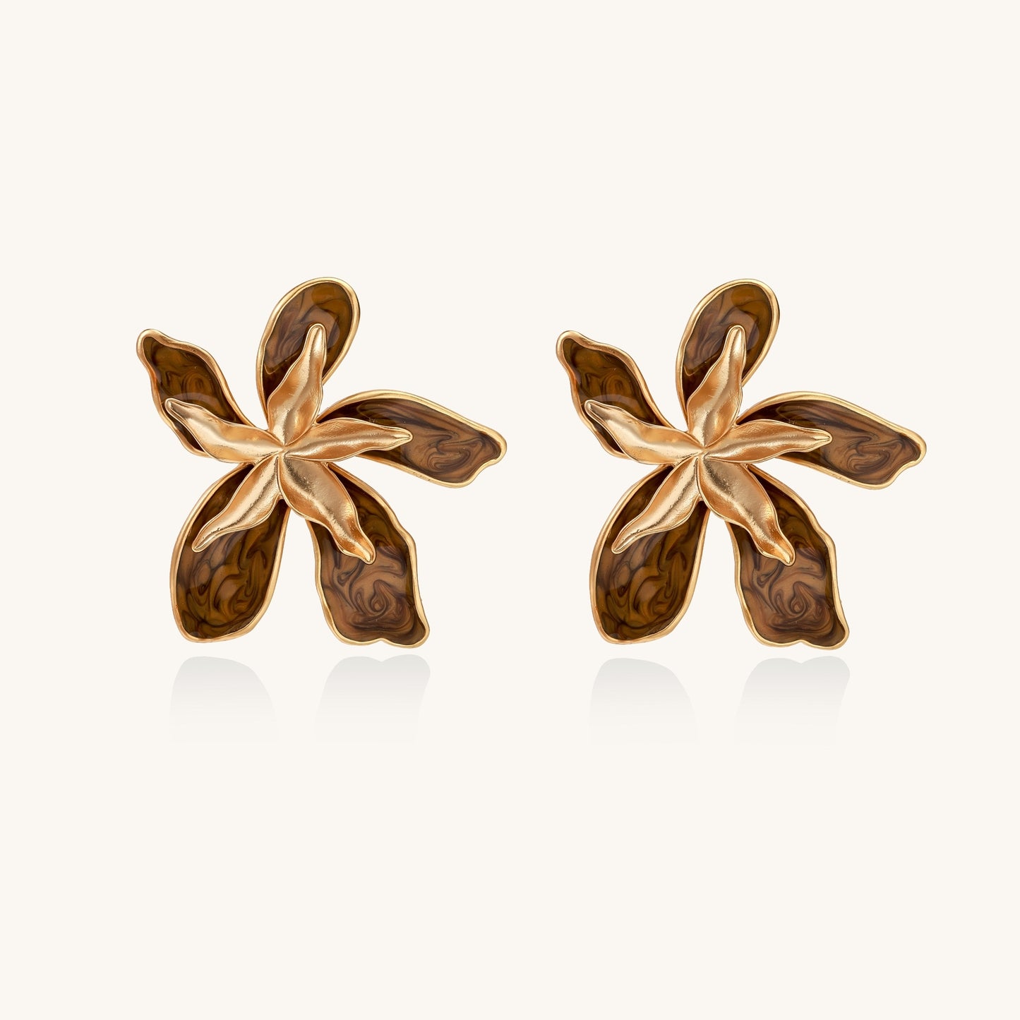 Large gold-plated flower earrings with brown enamel marbled petals on beige background, showing intricate floral design.