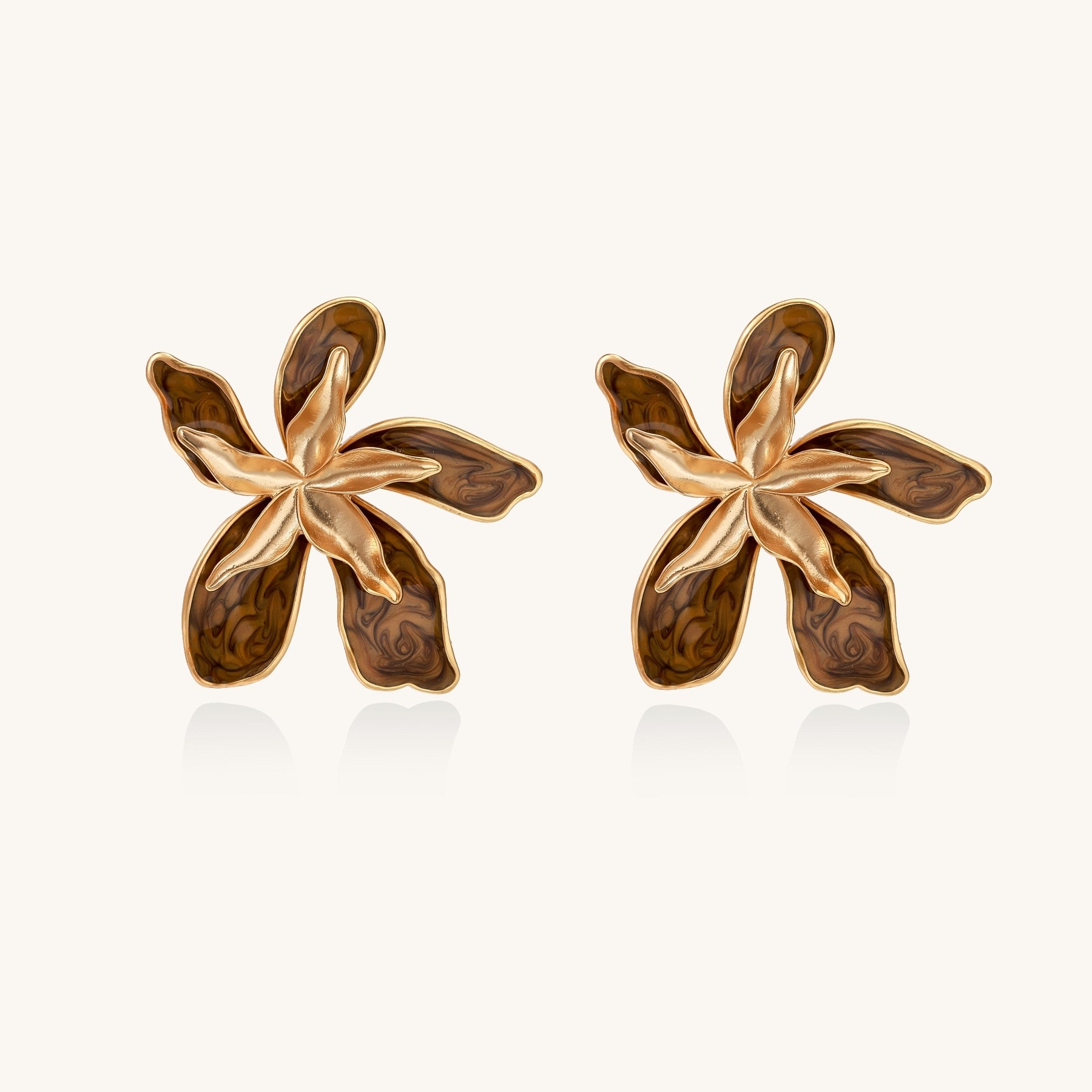 Large gold-plated flower earrings with brown enamel marbled petals on beige background, showing intricate floral design.