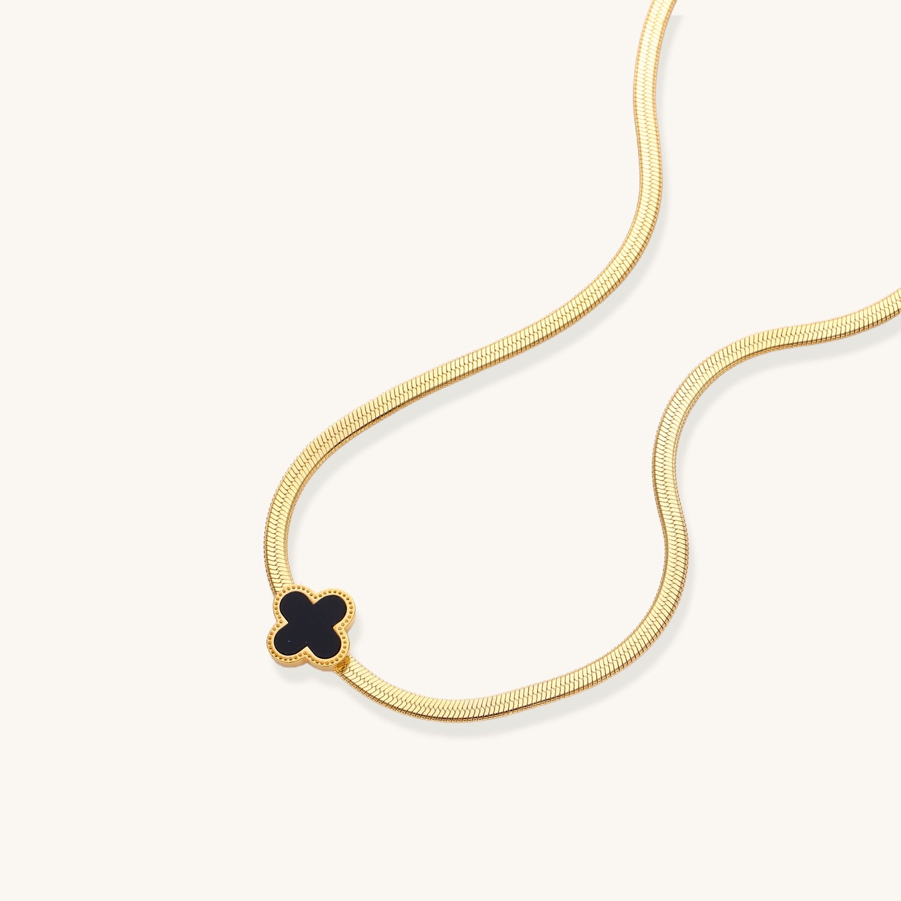 Delicate gold-plated chain necklace featuring a black quatrefoil clover pendant on white background.