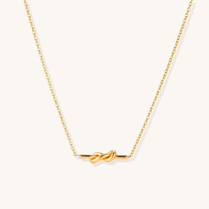 Dainty 18K gold plated stainless steel chain necklace with minimalist knot pendant on cream background.