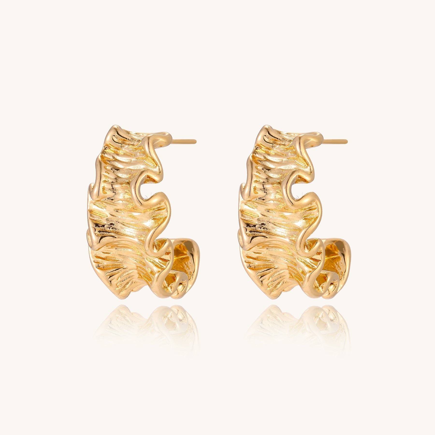 Close-up of dimensional gold-plated hoop earrings with rippled wave texture against white background.