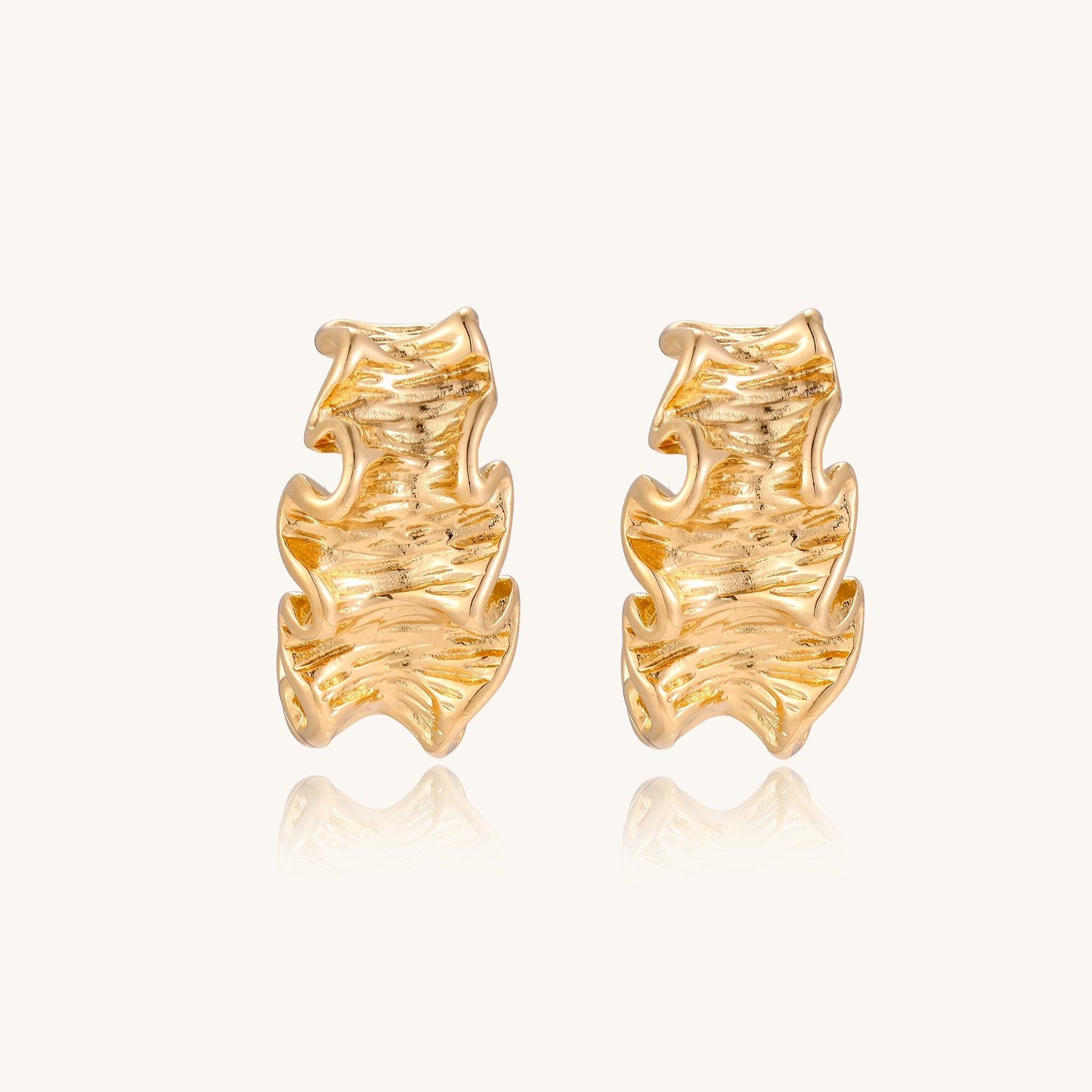 Close-up of dimensional gold-plated hoop earrings with rippled wave texture against white background.