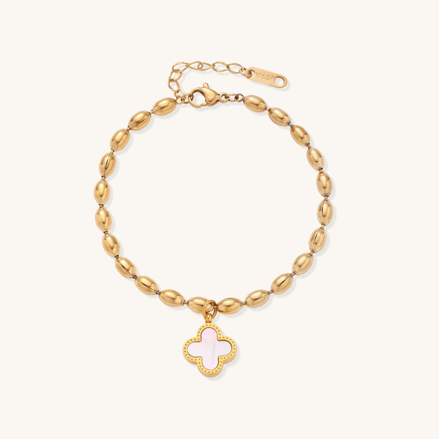 Dainty gold-plated beaded bracelet with oval links and four-leaf clover charm pendant on neutral background.