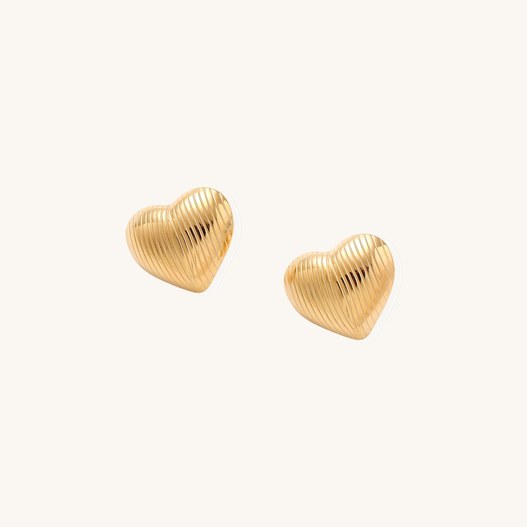 Close-up of ridged heart-shaped gold-plated stud earrings with textured surface pattern on cream background.