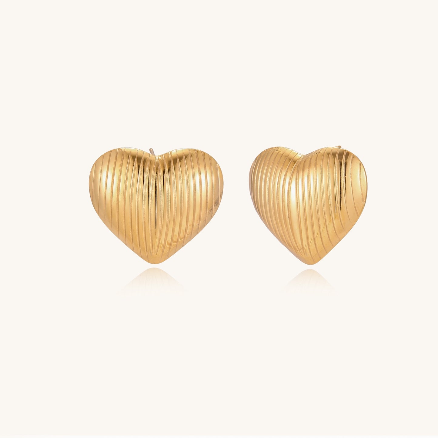Close-up of ridged heart-shaped gold-plated stud earrings with textured surface pattern on cream background.