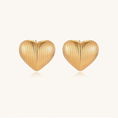 Close-up of ridged heart-shaped gold-plated stud earrings with textured surface pattern on cream background.