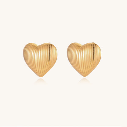 Close-up of ridged heart-shaped gold-plated stud earrings with textured surface pattern on cream background.