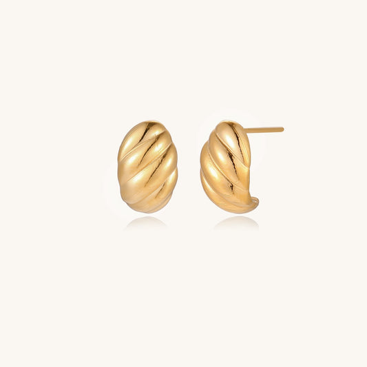 Pair of gold-plated twisted stud earrings with sculptural spiral design displaying elegant curved ridges on cream background.