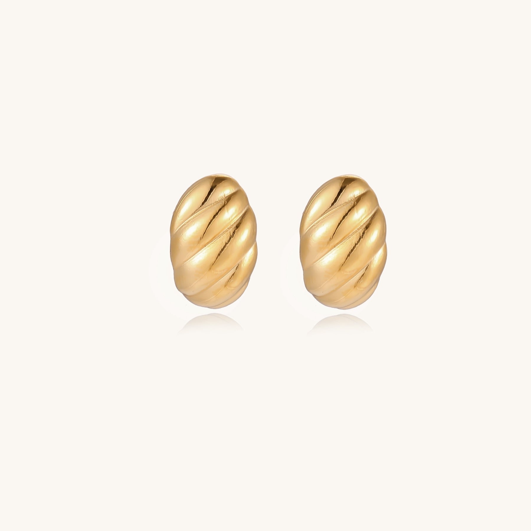 Pair of gold-plated twisted stud earrings with sculptural spiral design displaying elegant curved ridges on cream background.
