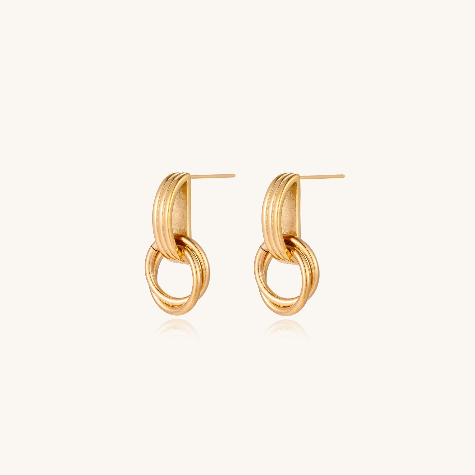 Geometric gold earrings with ribbed linear top section and circular drop elements on white background.