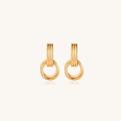 Geometric gold earrings with ribbed linear top section and circular drop elements on white background.