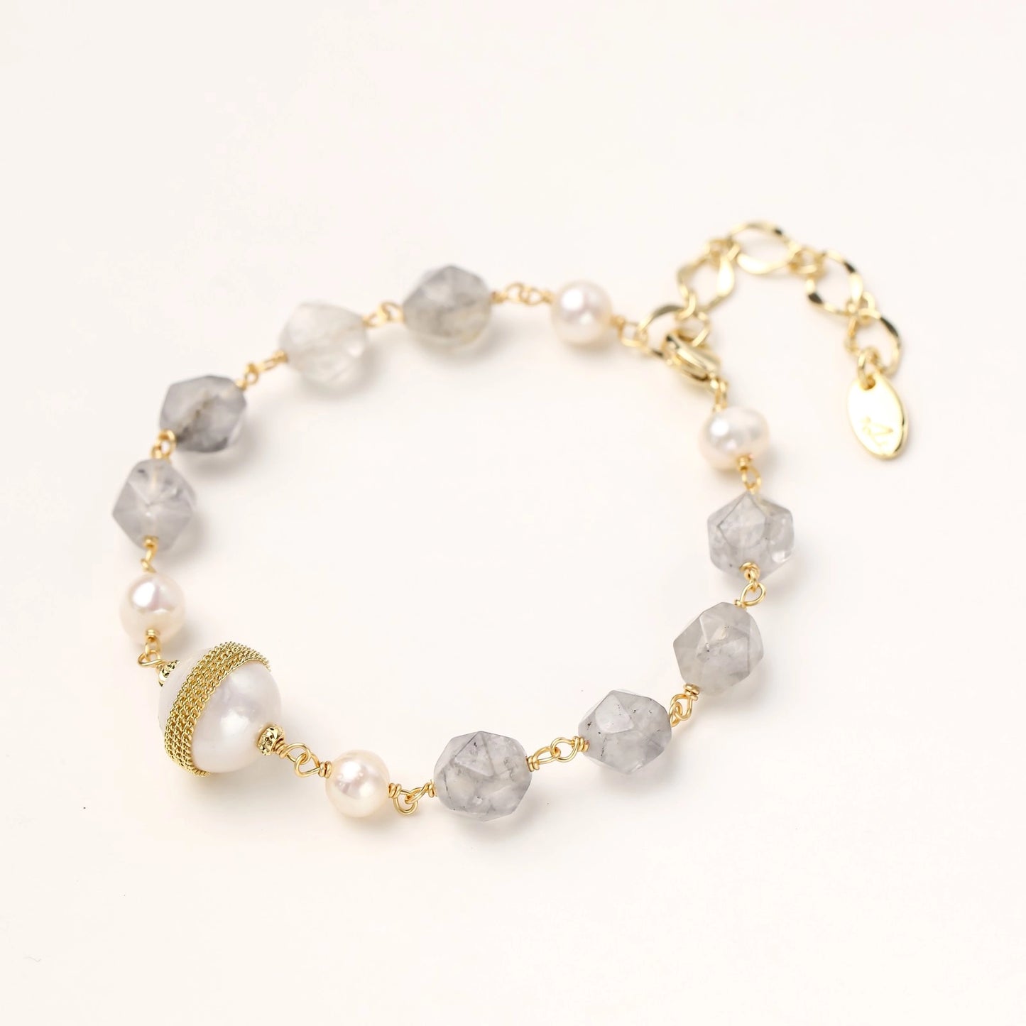 Gold-plated bracelet with white freshwater pearls and translucent grey crystals, featuring mesh-wrapped baroque pearl centerpiece