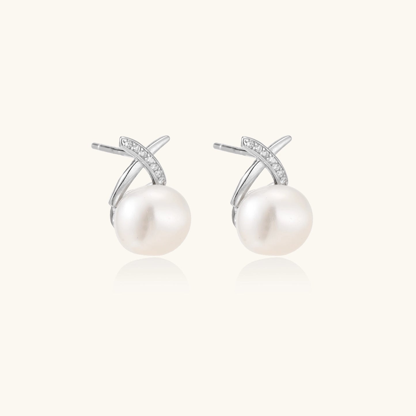 Sterling silver cross-shaped stud earrings with round freshwater pearls dangling below on white background.