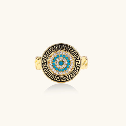 Gold-plated brass ring with Greek key border, evil eye center, and turquoise cubic zirconia stones in chunky chain band style.