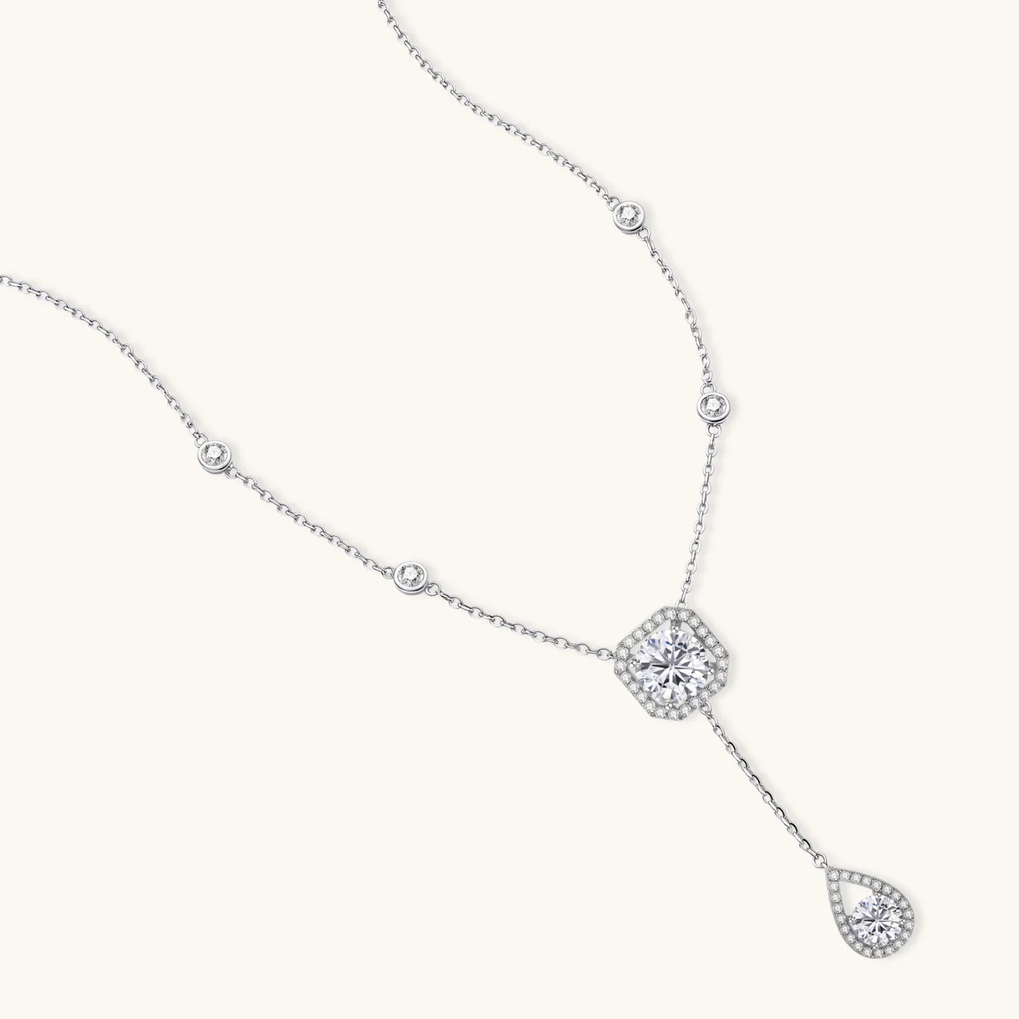 Sterling silver necklace with cushion-cut moissanite in halo setting and teardrop pendant, displayed on cream background.