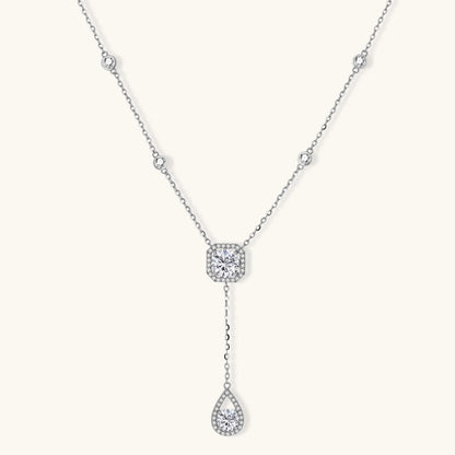 Sterling silver necklace with cushion-cut moissanite in halo setting and teardrop pendant, displayed on cream background.