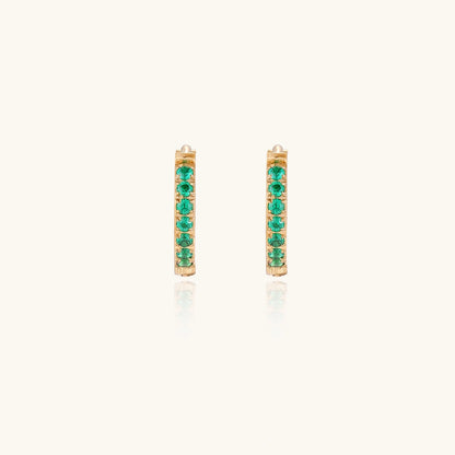 Pair of small gold huggie hoop earrings with bright green cubic zirconia stones on cream background