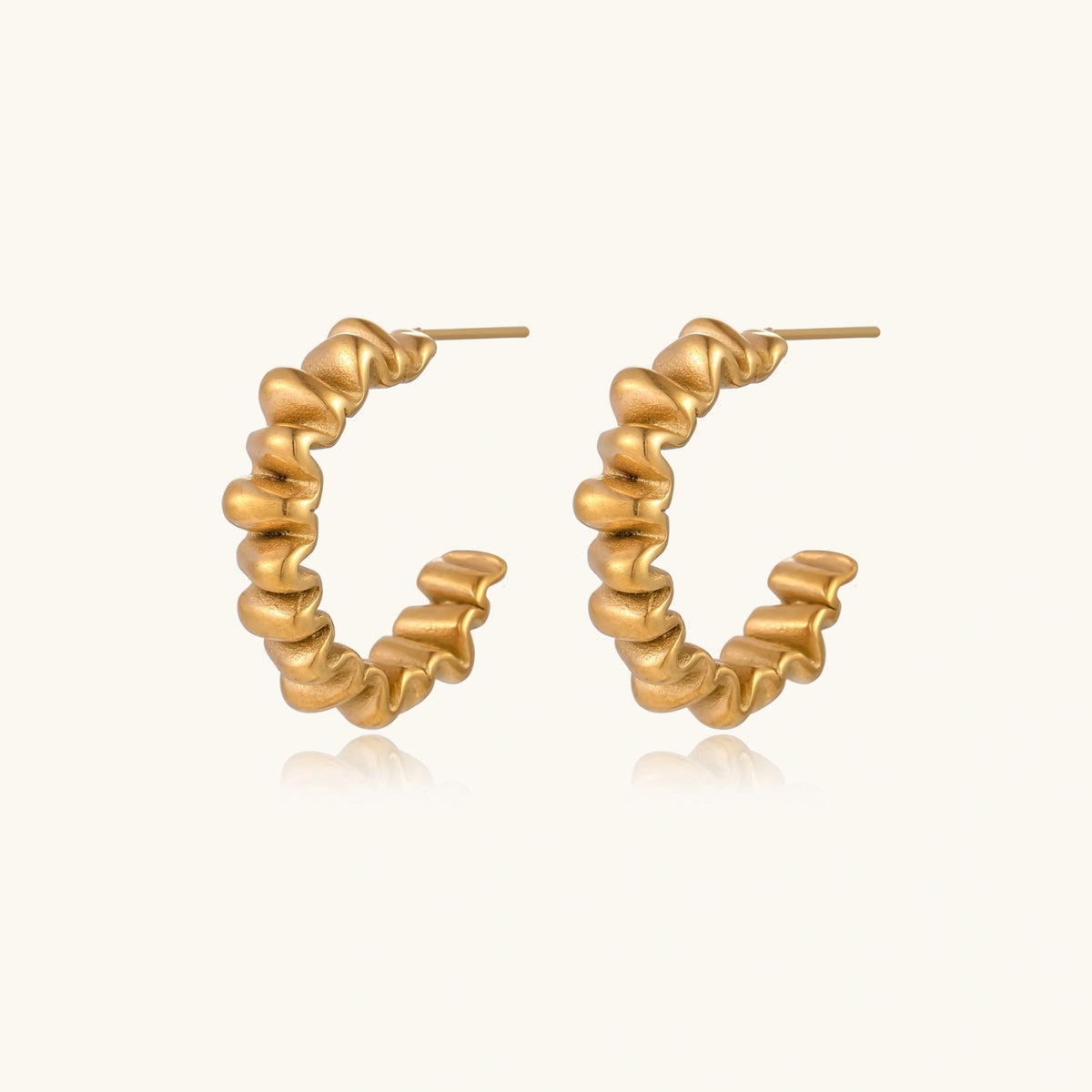 Sculptural gold-plated hoop earrings with continuous twisted spiral design on cream background
