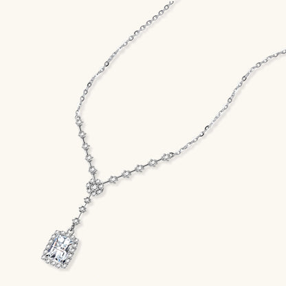 Sterling silver Y-necklace with rectangular moissanite pendant in halo setting and cascading accent stones on white background.