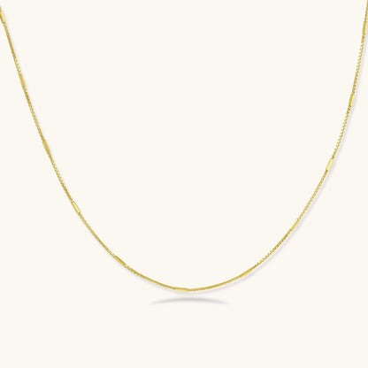 Delicate gold-plated sterling silver chain necklace with geometric segments displayed against cream background