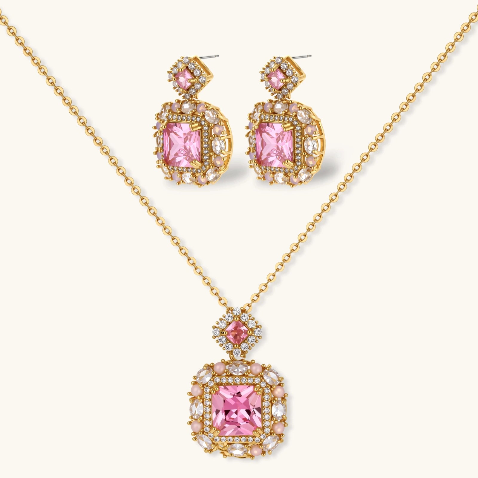 Ornate gold-plated jewelry set with rose pink zirconia center stones and crystal accents on cream background.