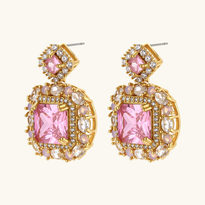 Ornate gold-plated jewelry set with rose pink zirconia center stones and crystal accents on cream background.